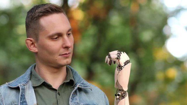 Young Man Looks on His Robotic Hand in the Park. Beautiful realistic 3d animation. 4K