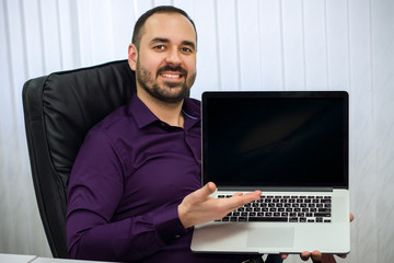 man sitting in armchair, smiling and showing his hand on laptop