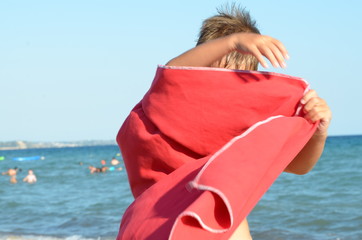 Child playing with a red towel on the bach