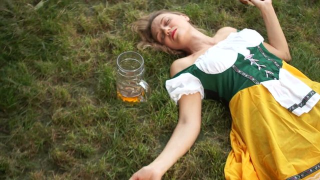 A lovely waitress in a national Bavarian dress at the Oktoberfest festival has drunk too much beer and is sleeping on the grass