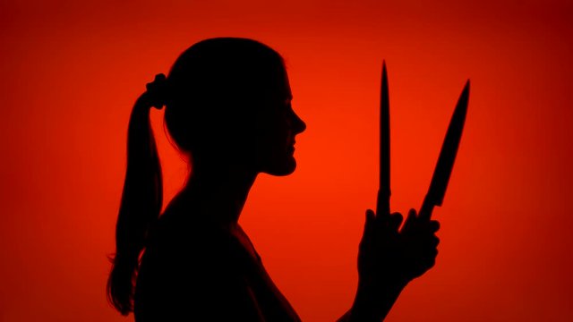 Silhouette of young scary woman holding sharp blades. Female's face in profile with two dangerous knives on red background. Black contour shadow of teenager's half-face. Violence and aggression