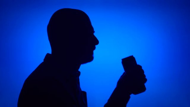 Silhouette of senior man opening can of beer on blue background. Male's face in profile drinking soda from tin. Black contur shadow of grandfather's half-face
