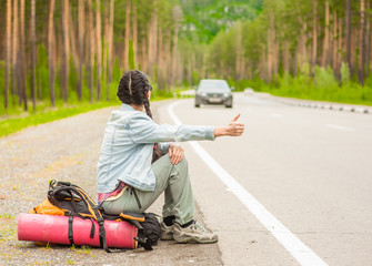 young woman  sitting on a backpack and  hitchhiking on the road