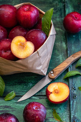 Red plums in a basket and scattered on a rustic base. Knife and cutted plum to show the inside