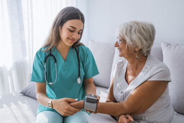Happy senior woman having her blood pressure measured in bed in a nursing home by her caregiver.