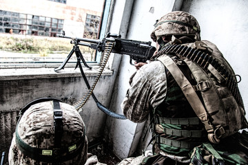 Marine Corps machine gun crew shooting through window in ruined building during city firefight....