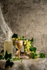 still life of two glasses of white wine one fall down and white wine spilled out to lace cloth with white wine bottle and green grapes