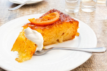 A piece of traditional greek orange cake on white plate. A mouthful of cake and sour cream on fork.