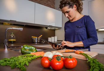 Young girl in home kitchen preparing food and looking recipe in a electronic tablet. Modern lifestyle concept.