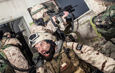 Special forces team leader screaming in tactical radio handset while coordinating allies actions,...