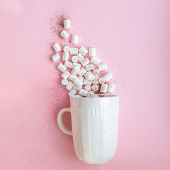 marshmallow poured from a white mug on a pastel pink background