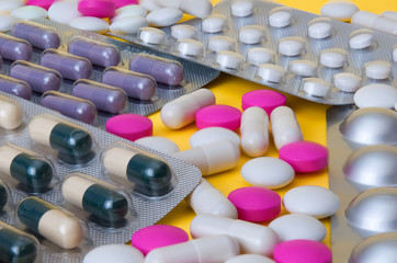 White and pink tablets and blisters with colorful pills are scattered. Side view.