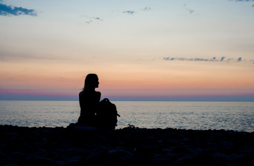 Happy carefree woman enjoying beautiful sunset on the beach. Profile of a young woman silhouette  sitting and watching on the sun. Vacation travel holidays and summer time concept
