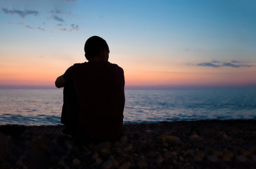 the man is sitting on the seashore and watching the sunset