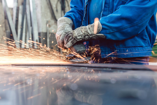 Metallarbeiter in Fabrik schleift Werkst&uuml;ck und Funken fliegen