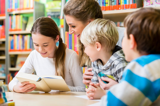 Lehrerin mit ihrer Klasse liest B&uuml;cher in der Bibliothek 