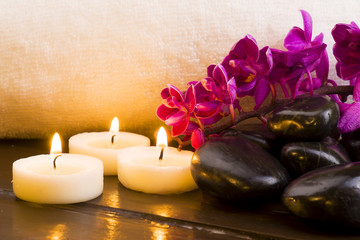 Fototapeta na wymiar Dark stones and candles and orchid on a white towel background