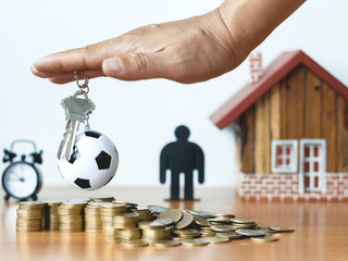 Real estate or property investment concept. Man's hand holds the house key, coin stack with house model on table.