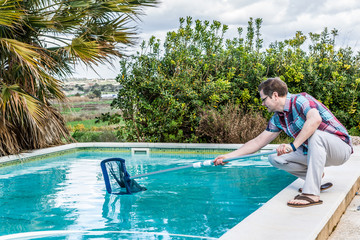 Mann hockt am Rand eines Pools mit einem Pool Cacher und fischt das Laub raus, closeup