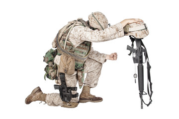 Army soldier in sorrow for fallen comrade, standing on knee, leaning on rifle with helmet and two...