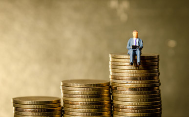 miniature figure business man sitting on top of pile stack of golden coins. business success concept
