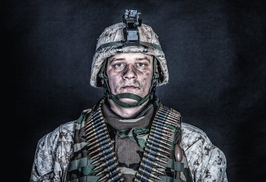 Shoulder portrait of experienced army soldier, military conflict veteran, skilled marine fighter in ragged camouflage uniform, advanced helmet and ammo belts on chest, studio shot on black background