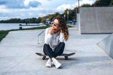 Cute girl with curly hair with skateboard in the park