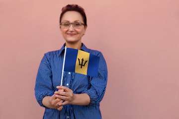 Barbados flag. Woman holding  Barbados flag. Nice portrait of middle aged lady 40 50 years old with a national flag over pink wall background outdoors.