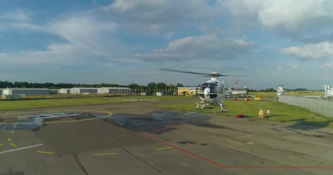 A white private helicopter takes off from the helipad at the airport and fly away.