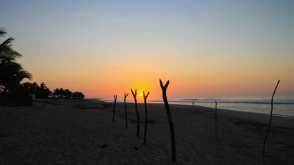 Tropical Sunrise over Fishing Net Drying Posts on Pacific Ocean Beach.