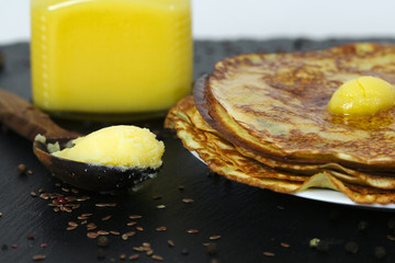 Pancakes are abundantly covered with creamy melted butter on a stone tray and a jar with butter
