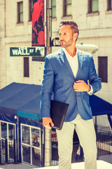 Young European Businessman with beard traveling, working in New York City, wearing blue blazer, white shirt, holding briefcase, standing on street outside office by Wall Street sign, looking forward..