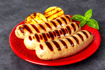 Three sausages of pork and zucchini on a red plate. Basil. Background black marble.
