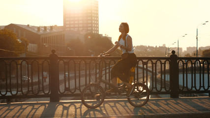Red haired woman riding a bicycle on background sunlight in city