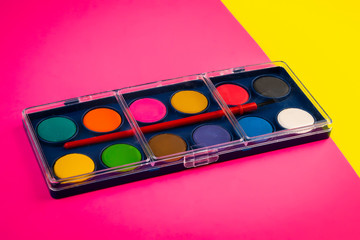 box with watercolors and brush on colored sheets of paper