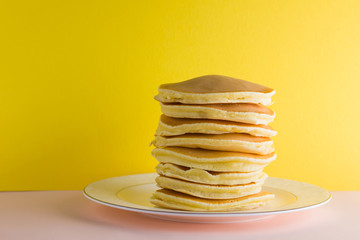 Pancakes on a yellow pink background. Many pancakes on a white plate with copy space. Delicious dish for breakfast in the style of pop art. Festive food on a colorful background. French breakfast