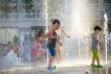 Happy kids have fun playing in city water fountain on hot summer day.