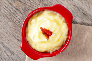 Puree from potatoes in a red saucepan. Red pepper in the middle of the dish. Wooden background. Macro.