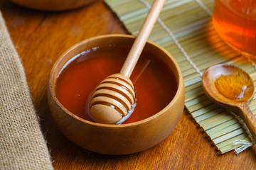 Honey in wooden bowl with honey dipper on wooden table