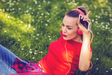 Happy woman with earphones and smartphone listening to music on grass.