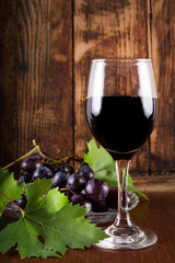 Red wine in glass and grape on plate with vine decoration. Wooden retro brown background and desk. Vintage food and drink concept. Close up, selective focus