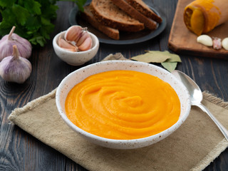 carrot puree, mashed of roasted carrot in white plate on a dark wooden background, side view