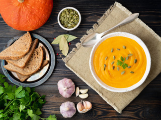 pumpkin soup mashed in a white plate, pumpkin seeds, bread, garlic on a dark wooden background, top view.