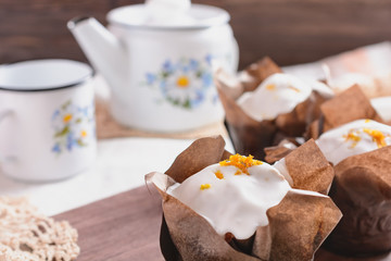 Freshly baked muffins in a paper wrapper are ready for eating, and next to a country style white teapot and a cup