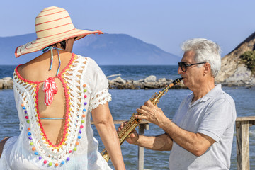 Senior man playing saxophone for his wife on the beach, leisure time