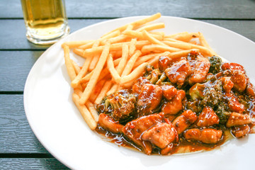 Stir-fried or wok fish with colorful vegetables and cabbage, soy sauce and seeds, french fries on a wooden table with beer in the background