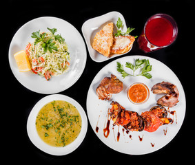 Delicious dinner table with grilled meat and vegetables, fresh vegetables salad, chicken soup, toast with cheese and compote