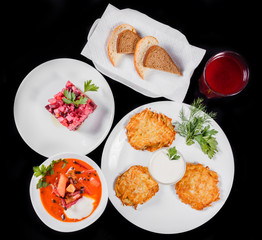 Delicious dinner table with potato pancakes, traditional beetroot soup - borscht with beef, beet salad Vinaigrette