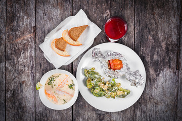 Delicious dinner table with baked meat and broccoli, fish soup with salmon and prawn, bread and compote on wooden background