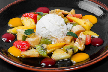 Fruit salad with banana, kiwi, orange, grapefruit in pineapple on plate over dark background. Healthy breakfast.
